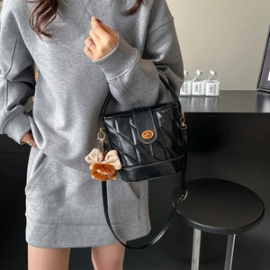 Sac seau matelassé noir avec fermoir doré et breloque peluche porté à l'épaule