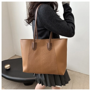 Detail of tan patchwork tote bag with faux snake skin texture shown on a shoulder