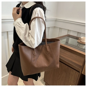 Detail of a large brown tote bag with snake pattern texture on a shoulder strap model