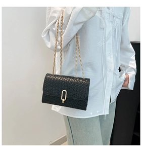 Detail of black woven texture bag featuring golden chain straps and oval clasp on shoulder