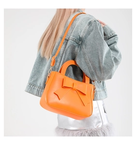 Modella che indossa una borsa a tracolla arancione con fiocco su una giacca di denim