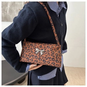 Detail of leopard print underarm bag with silver butterfly hardware on model's shoulder