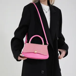 Pink baguette shoulder bag with woven flap and gold hardware held by model in black suit