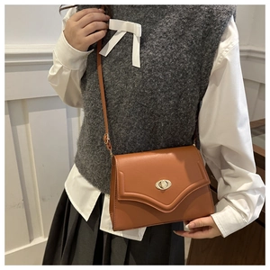 Detail of tan leather crossbody bag featuring an envelope flap and gold twist-lock closure