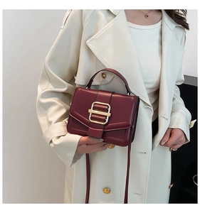 Detail of wine red handbag with gold buckle closure and sleek leather finish