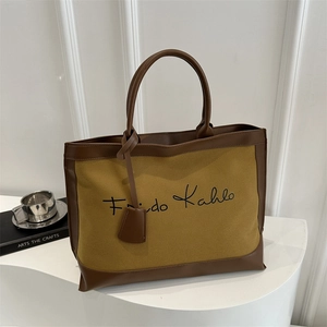 Detail of canvas tote bag with brown leather trim and Frida Kahlo script lettering