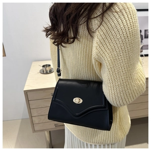 Detail of black matte envelope bag with a golden oval rotating buckle on cream sweater