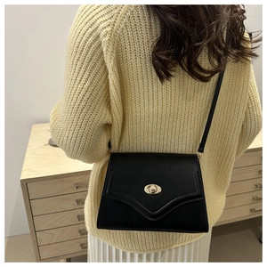 Detail of black leather shoulder bag with golden oval swivel lock worn by a model