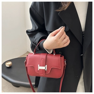 Detail of red leather crossbody bag featuring silver H-shaped buckle on a black suit