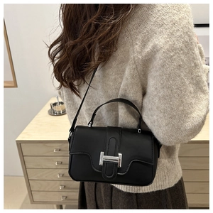 Macro detail of silver H-shaped buckle on minimalist black leather crossbody bag