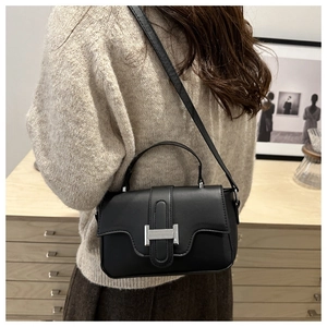 Detailed shot of matte black leather bag with silver H-buckle worn on a shoulder