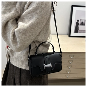 Detail of a black leather crossbody bag with a silver H-buckle and adjustable strap