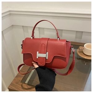 Close-up of deep red leather handbag featuring silver buckle and adjustable strap on a desk