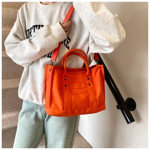 Detail of bright orange canvas tote bag showing reinforced stitching and metal studs