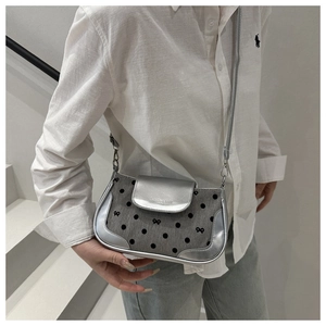 Sac bandoulière en cuir argenté et denim gris à pois noirs porté par une femme mannequin