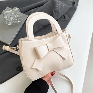 Elegante borsa a mano color crema con grande fiocco e tracolla in un ambiente moderno