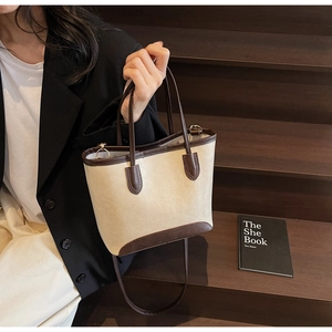 Detail of cream bucket bag with brown leather trim and texture on wooden steps