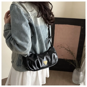 Detail of black pleated underarm bag featuring a metallic gold triangle logo and glossy finish