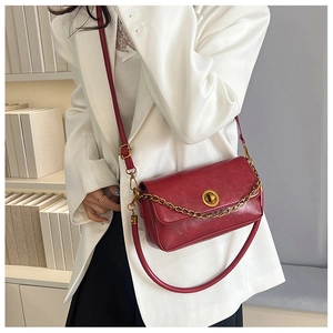 Détail d'un sac bandoulière vintage en cuir rouge avec chaîne dorée et boucle métallique