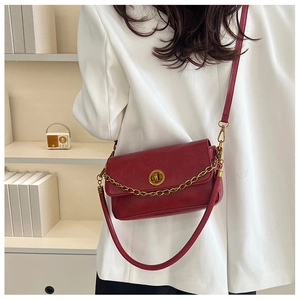 Détail d'un sac à main vintage en cuir rouge foncé avec chaîne sur un blazer blanc pur