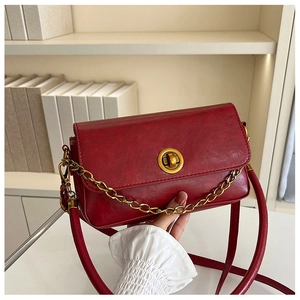 Détail d'un sac en similicuir rouge avec fermoir pivotant doré et décorations de chaîne