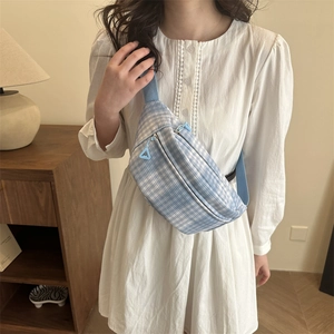 Light blue plaid corduroy waist bag with adjustable strap worn by model in a cozy room