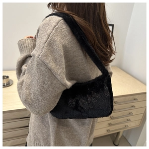 Detailed close-up of a soft black faux fur shoulder bag worn by a model in a cozy setting