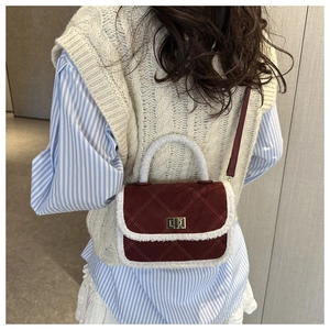 Detailed close-up of dark red suede crossbody bag with white faux fur trim and gold buckle
