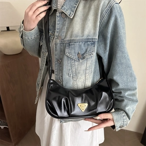 Glossy black pleated crescent underarm bag with gold triangular logo on model