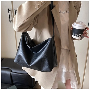 Chic black slouchy tote bag in glossy leather carried by a model in a beige blazer