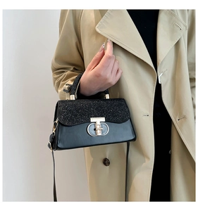 Detail of elegant black handbag featuring sequin flap, golden T-buckle and top handle