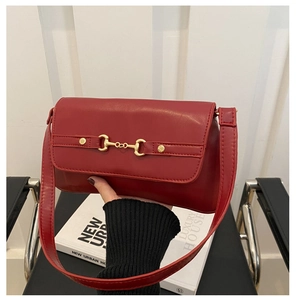 Detail of red rectangular leather shoulder bag with gold horsebit buckle on white books