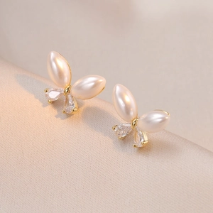 Elegant butterfly stud earrings with pearls and crystals on champagne silk background