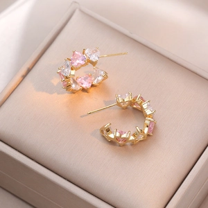 Elegante goldene C-Ohrringe mit rosa und klaren Herz-Zirkonia in einer beigen Schmuckbox