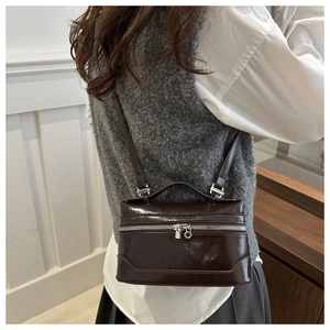 Detail of dark brown glossy patent leather box bag with top handle and shoulder strap