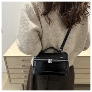 Polished black patent leather box crossbody bag with silver zippers shown on a model
