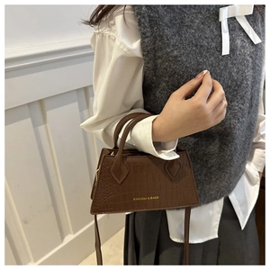 Detail of dark brown crocodile pattern handbag with elegant curved handle and gold logo