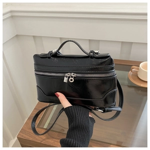Detail of glossy black patent leather box bag with silver metal zippers and charms