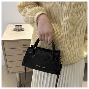 Close-up of black crocodile pattern small square handbag with gold lettering and top handle