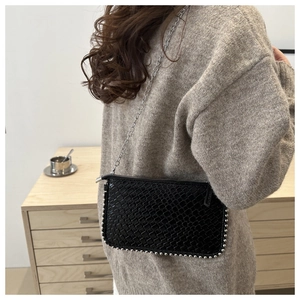 Detail of black woven leather crossbody bag with silver stud trim and chain strap
