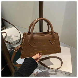 Detailed view of the brown crocodile pattern texture and gold logo on the handbag
