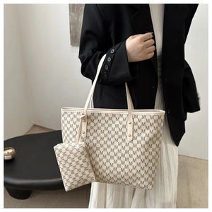 Detail of a beige tote bag set with dark M-pattern print and gold metal hardware