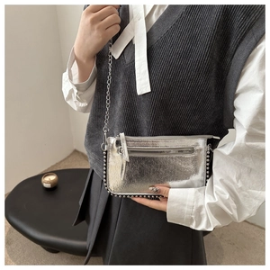 Detail of silver metallic crossbody bag featuring metal studs and a chain shoulder strap