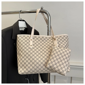 Detail of a beige tote bag set with M-letter pattern and golden rivet accents