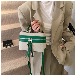 Detail of beige canvas crossbody bag with green leather trim and dual zipper design