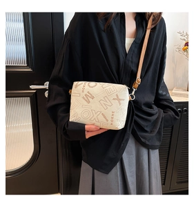 Modèle portant un sac bandoulière blanc crème avec motifs lettres et détails dorés