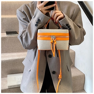 Detail of a chic rectangle box bag with orange leather trim and beige canvas panels