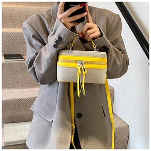Detail view of small square canvas box bag with bright yellow fringe and zipper accents