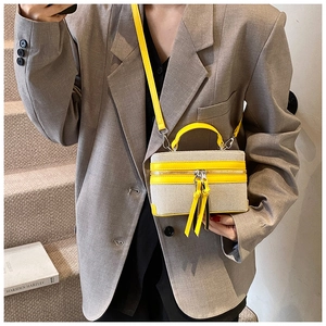 Detail of a beige canvas box bag with bright yellow leather trim and dual fringe tassels