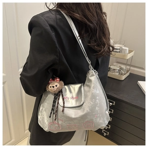 Detail der silbernen Metallic-Tasche mit rosa Drucken und Plüschbär-Anhänger am Gurt